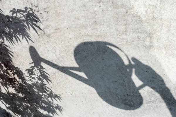Shadow silhouette of a hand holding a watering can on a grey wall