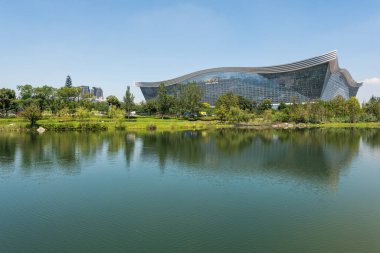 New Century Global Center binası açık mavi gökyüzü ile güneşli bir günde bir göle yansıyor.