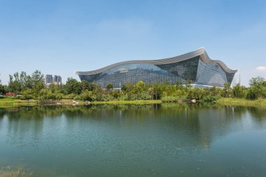 New Century Global Center binası açık mavi gökyüzü ile güneşli bir günde bir göle yansıyor.