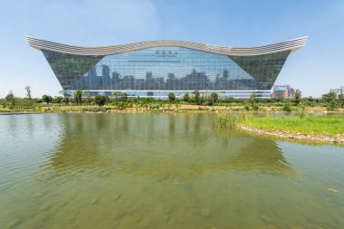New Century Global Center binası açık mavi gökyüzü ile güneşli bir günde bir göle yansıyor.