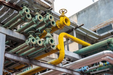 Parlak renkli borular bir sanayi bölgesinde görülüyor. Yapılar arasında karmaşık bir düzende birbirine bağlı yeşil ve sarı borular da yer alıyor.