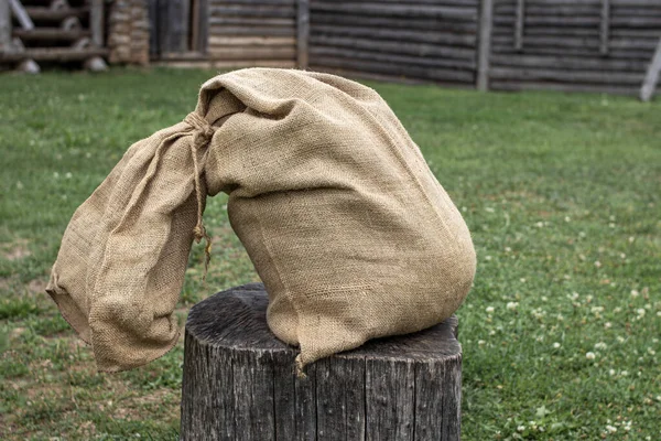 Yaşlı bir çuval yeşil bir çimenliğin ortasında, tahta bir kütüğün üzerinde yatıyor.