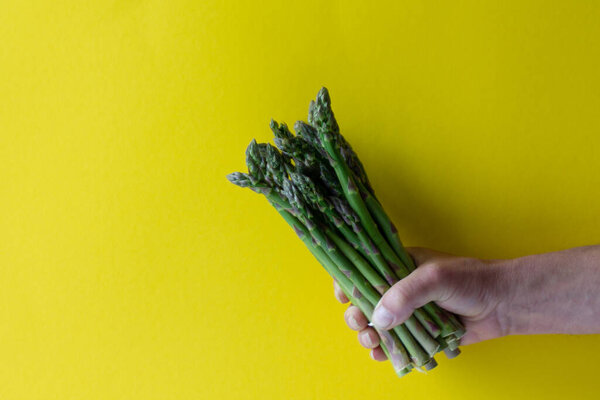 Спаржа в руках человека на жёлтом фоне. Питаться здоровой пищей
.