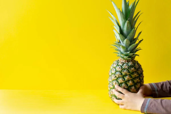 Sarı arka planda, çocuk eli olan lezzetli bir ananas.