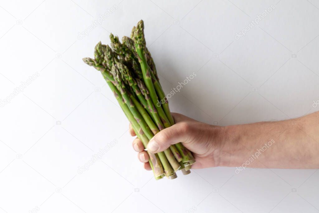 Asparagus in a mans hand on white background. To eat healthy food.