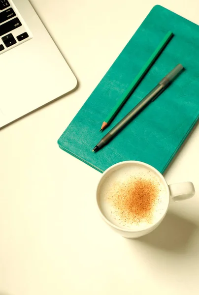 Spazio di lavoro con laptop, notebook turchese e caffè alla cannella su tavolo bianco. Posa piatta, vista dall'alto — Foto Stock