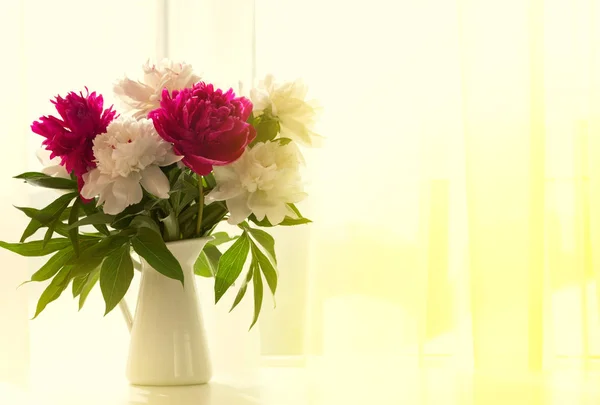 Белые и розовые пионы в вазе на белом столе — стоковое фото