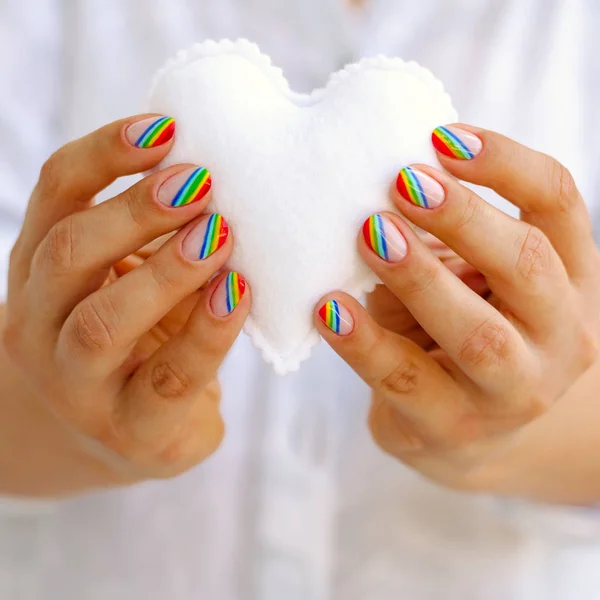 White felted heart in femaile hands with rainbow manicure. Love, valentine, lgbt, pride concept