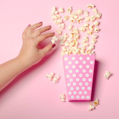 Pembe arka planda patlamış mısır olan karton kutu.