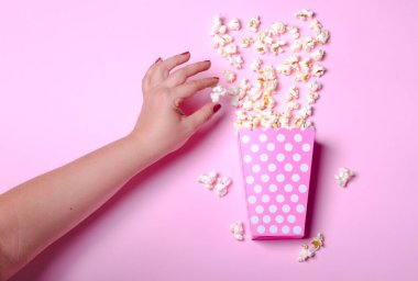 Pembe arka planda patlamış mısır olan karton kutu.