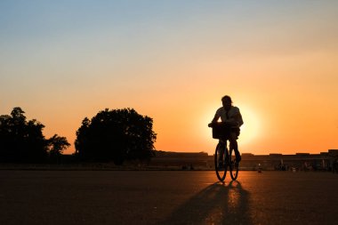 Günbatımı arka planında bisiklet süren bir kişinin silueti.