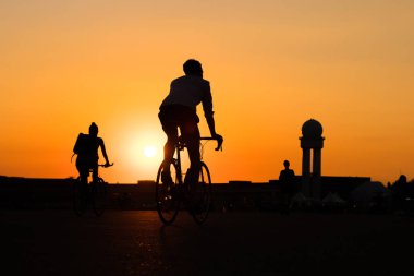 Günbatımı arka planında bisiklet süren genç bir adamın silueti. -