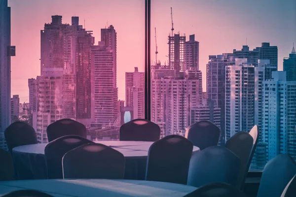 empty dinner table in room with view over modern skyline during sunset -