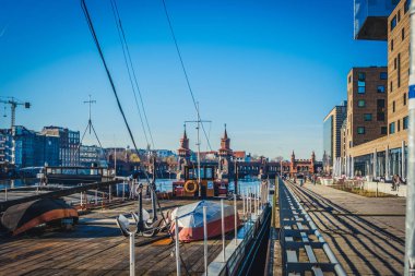Berlin 'de yaz mevsimi nehir kıyısında Oberbaaum Köprüsü, tekne ve sahil kenarındaki insanlarla dolu. -