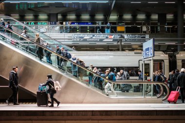 Ana tren istasyonunda yürüyen merdivende bavulları olan insanlar.
