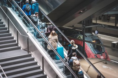 Ana tren istasyonunda yürüyen merdivende bavulları olan insanlar.