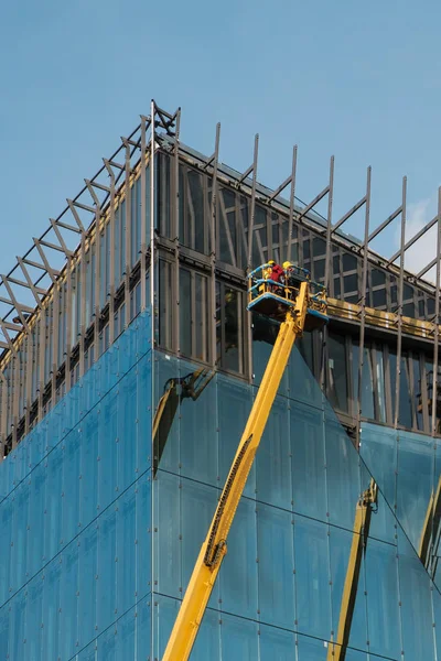 Kranen op glazen gevel kantoorgebouw in aanbouw - — Stockfoto