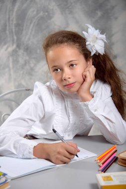 Kız öğrenci okulun Tekdüzen masada oturur ve hafif gri arka plan üzerinde görev kararı hakkında düşünüyor. Okula dönüş. Yeni öğretim yılı. Çocuk eğitim kavramı.