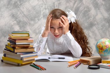 Kız öğrenci okulun Tekdüzen masada oturur ve hafif bir gri arka plan üzerinde sert ve zor bir görev karar hakkında düşünüyor. Okula dönüş. Yeni öğretim yılı. Çocuk eğitim kavramı.