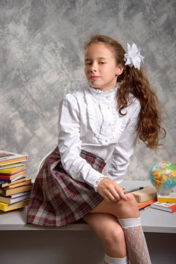 Topluca kız öğrenci okulun Tekdüzen tablo ve gülümseyerek mutlu bir şekilde ışık gri arka plan üzerinde oturur. Okula dönüş. Yeni öğretim yılı. Çocuk eğitim kavramı.