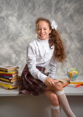 Topluca kız öğrenci okulun Tekdüzen tablo ve gülümseyerek mutlu bir şekilde ışık gri arka plan üzerinde oturur. Okula dönüş. Yeni öğretim yılı. Çocuk eğitim kavramı.