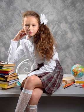 Topluca kız öğrenci okulun Tekdüzen tablo ve gülümseyerek mutlu bir şekilde ışık gri arka plan üzerinde oturur. Okula dönüş. Yeni öğretim yılı. Çocuk eğitim kavramı.