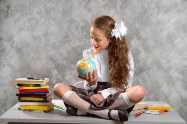 Topluca kız öğrenci okulun Tekdüzen tablo ve gülümseyerek mutlu bir şekilde ışık gri arka plan üzerinde oturur. Okula dönüş. Yeni öğretim yılı. Çocuk eğitim kavramı.