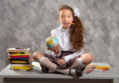 Topluca kız öğrenci okulun Tekdüzen tablo ve gülümseyerek mutlu bir şekilde ışık gri arka plan üzerinde oturur. Okula dönüş. Yeni öğretim yılı. Çocuk eğitim kavramı.