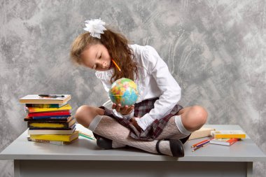 Topluca kız öğrenci okulun Tekdüzen tablo ve gülümseyerek mutlu bir şekilde ışık gri arka plan üzerinde oturur. Okula dönüş. Yeni öğretim yılı. Çocuk eğitim kavramı.