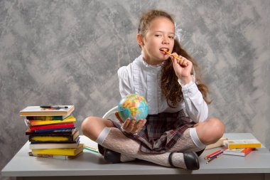 Topluca kız öğrenci okulun Tekdüzen tablo ve gülümseyerek mutlu bir şekilde ışık gri arka plan üzerinde oturur. Okula dönüş. Yeni öğretim yılı. Çocuk eğitim kavramı.