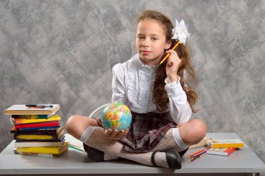 Topluca kız öğrenci okulun Tekdüzen tablo ve gülümseyerek mutlu bir şekilde ışık gri arka plan üzerinde oturur. Okula dönüş. Yeni öğretim yılı. Çocuk eğitim kavramı.