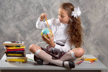 Topluca kız öğrenci okulun Tekdüzen tablo ve gülümseyerek mutlu bir şekilde ışık gri arka plan üzerinde oturur. Okula dönüş. Yeni öğretim yılı. Çocuk eğitim kavramı.