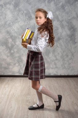 Kız öğrenci okul üniforma ile ışık gri arka plan üzerinde kitaplar ve ders kitapları teşkil etmektedir. Okula dönüş. Yeni öğretim yılı. Çocuk eğitim kavramı.