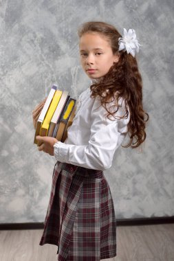 Kız öğrenci okul üniforma ile ışık gri arka plan üzerinde kitaplar ve ders kitapları teşkil etmektedir. Okula dönüş. Yeni öğretim yılı. Çocuk eğitim kavramı.