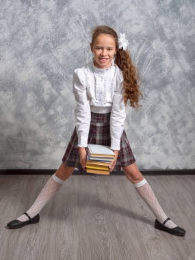 Kız öğrenci okul üniforma ile ışık gri arka plan üzerinde kitaplar ve ders kitapları teşkil etmektedir. Okula dönüş. Yeni öğretim yılı. Çocuk eğitim kavramı.