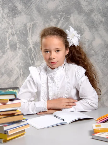 The schoolgirl in school uniform sits at the desk and and writes something in notebook. Back to school. The new school year. Child education concept.