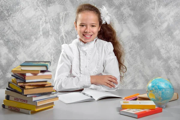 The schoolgirl in school uniform sits at the desk and and writes something in notebook. Back to school. The new school year. Child education concept.