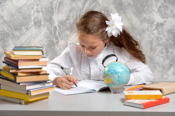 The schoolgirl in school uniform looking at a globe through a magnifying glass and writing something in a notebook. Back to school. The new school year. Child education concept. A geography lesson