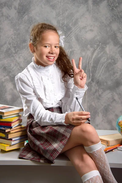 The fidget schoolgirl in school uniform sits on table and smiles happily on a light gray background. Back to school. The new school year. Child education concept.