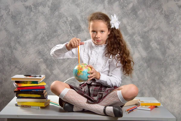 The fidget schoolgirl in school uniform sits on table and smiles happily on a light gray background. Back to school. The new school year. Child education concept.