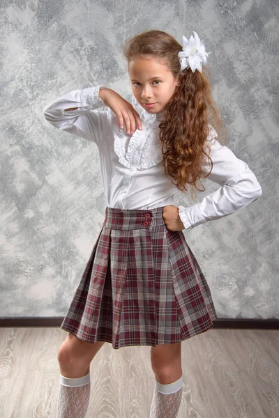 The schoolgirl in school uniform poses and has fun on a light gray background. Back to school. The new school year. Child education concept.