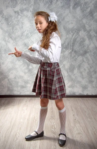 The schoolgirl in school uniform poses and has fun on a light gray background. Back to school. The new school year. Child education concept.