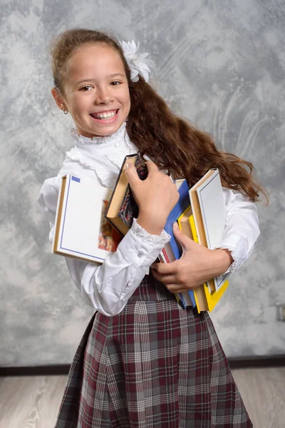 Kız öğrenci okul üniforma ile ışık gri arka plan üzerinde kitaplar ve ders kitapları teşkil etmektedir. Okula dönüş. Yeni öğretim yılı. Çocuk eğitim kavramı.