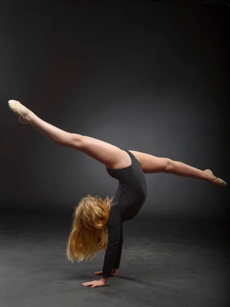 Joven hermosa blanca caucásica chica gimnasta con el pelo largo haciendo ejercicio gimnástico sobre fondo negro . —  Fotos de Stock