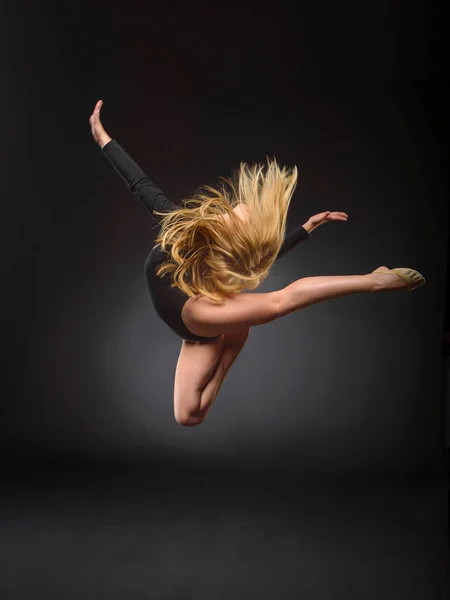 Young beautiful white caucasian girl gymnast with long hair jumps on black background. — Stock Photo, Image