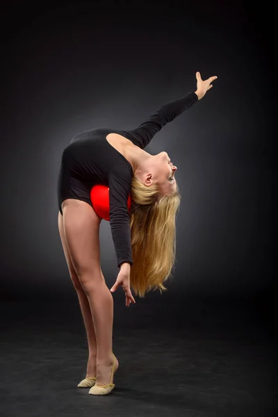 Joven hermosa blanca caucásica chica gimnasta con el pelo largo haciendo ejercicio gimnástico sobre fondo negro . — Foto de Stock