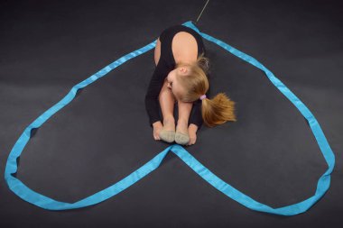 Beyaz güzel genç mavi kurdele ile katta oturan beyaz kız jimnastikçi. Kalp şeklinde jimnastik teyp