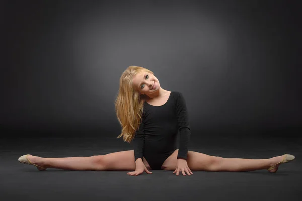 Hermosa chica blanca caucásica gimnasta haciendo ejercicio gimnástico para la flexibilidad y estiramiento sobre fondo negro . — Foto de Stock