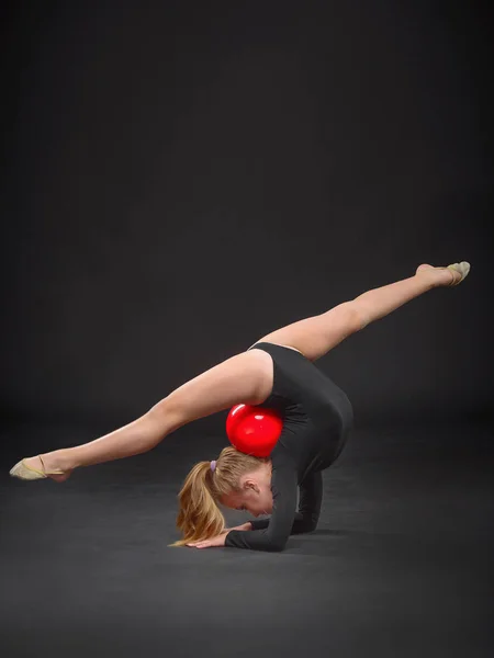 Joven hermosa blanca caucásica chica gimnasta haciendo ejercicio gimnástico con una pelota deportiva roja sobre fondo negro —  Fotos de Stock
