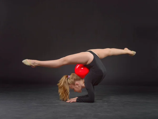 Fiatal gyönyörű fehér kaukázusi lány tornász csinál gimnasztikai gyakorlás-val a fekete háttér piros sport labda — Stock Fotó